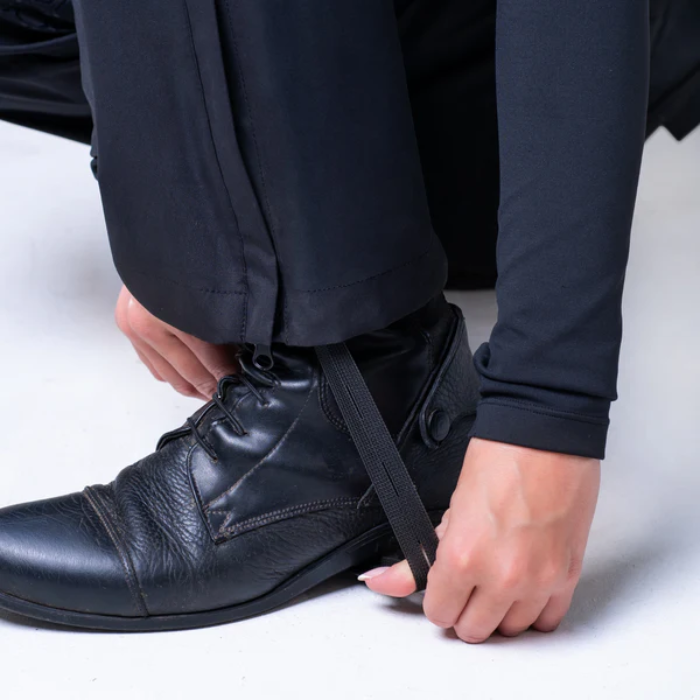 Person adjusting a black strap over a leather shoe on a light grey background