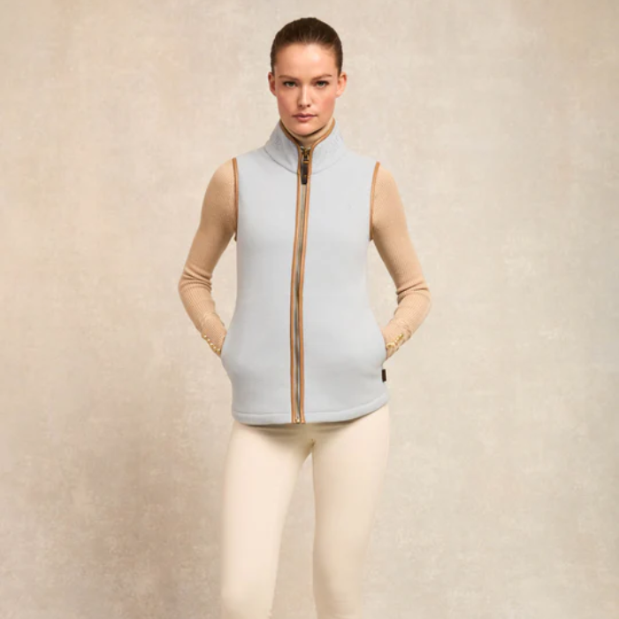 Woman wears a light blue fleece gilet and neutral top on a plain background