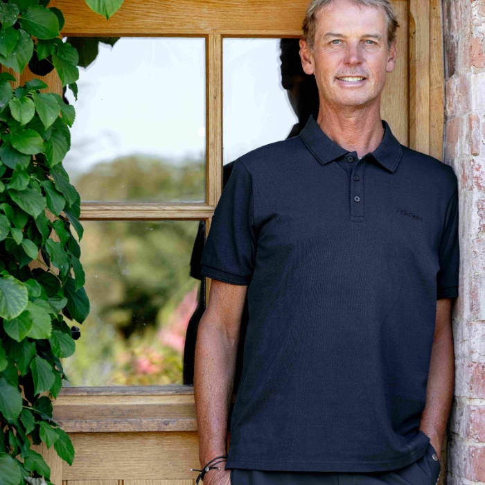 Man wears a navy blue polo t-shirt standing in a doorway with foliage