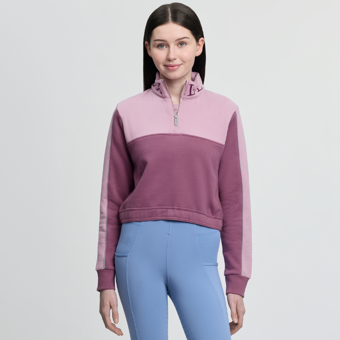 Woman wearing a two-tone pink and purple sweatshirt with blue leggings on a light grey background