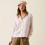 Woman wears a linen shirt and brown leather shorts on a plain background