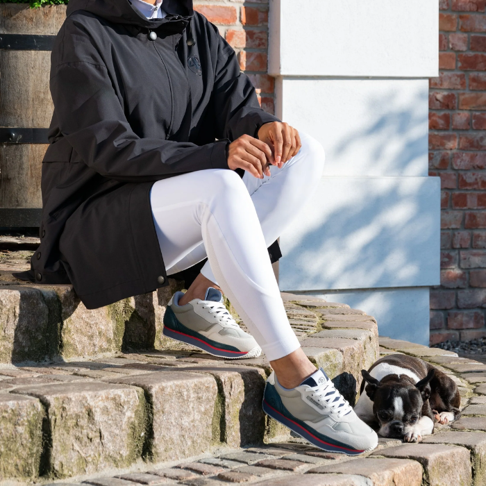 Person sitting on stone steps wearing a black coat, white pants, and sneakers with a dog lying next to them.