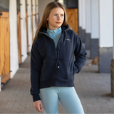 Woman wearing a navy hoodie with a brand logo, standing outdoors.