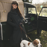 Woman standing next to a vintage vehicle with a dog on a leash in a natural setting