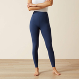 Person wears blue riding tights and a white top on a beige background and wooden floor