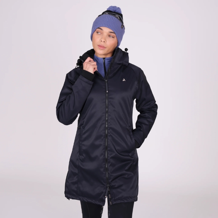 Woman wears a mid length black coat and blue wool hat on a light background