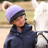 Person wearing a purple helmet and blue jacket standing next to a white horse.