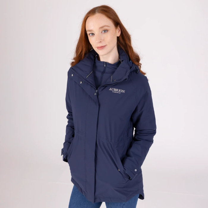 Woman wears a lightweight blue jacket with AUBRION branding on a light grey background