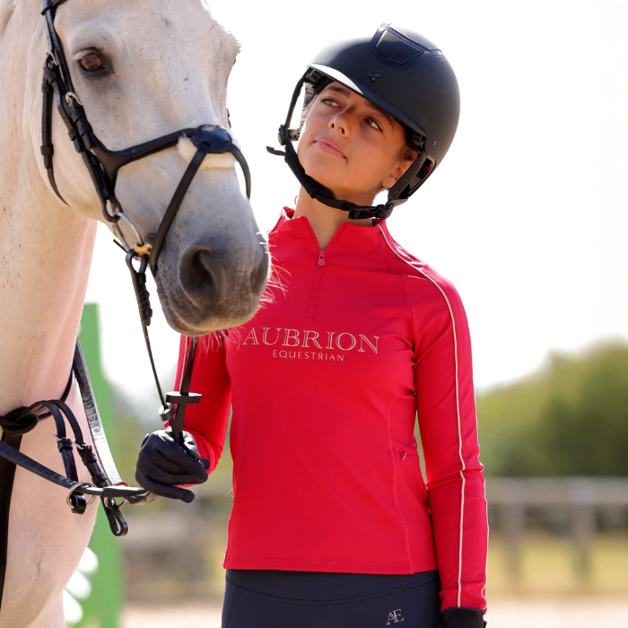Female wearing horse riding hat and pink long sleeve top holding a grey horse